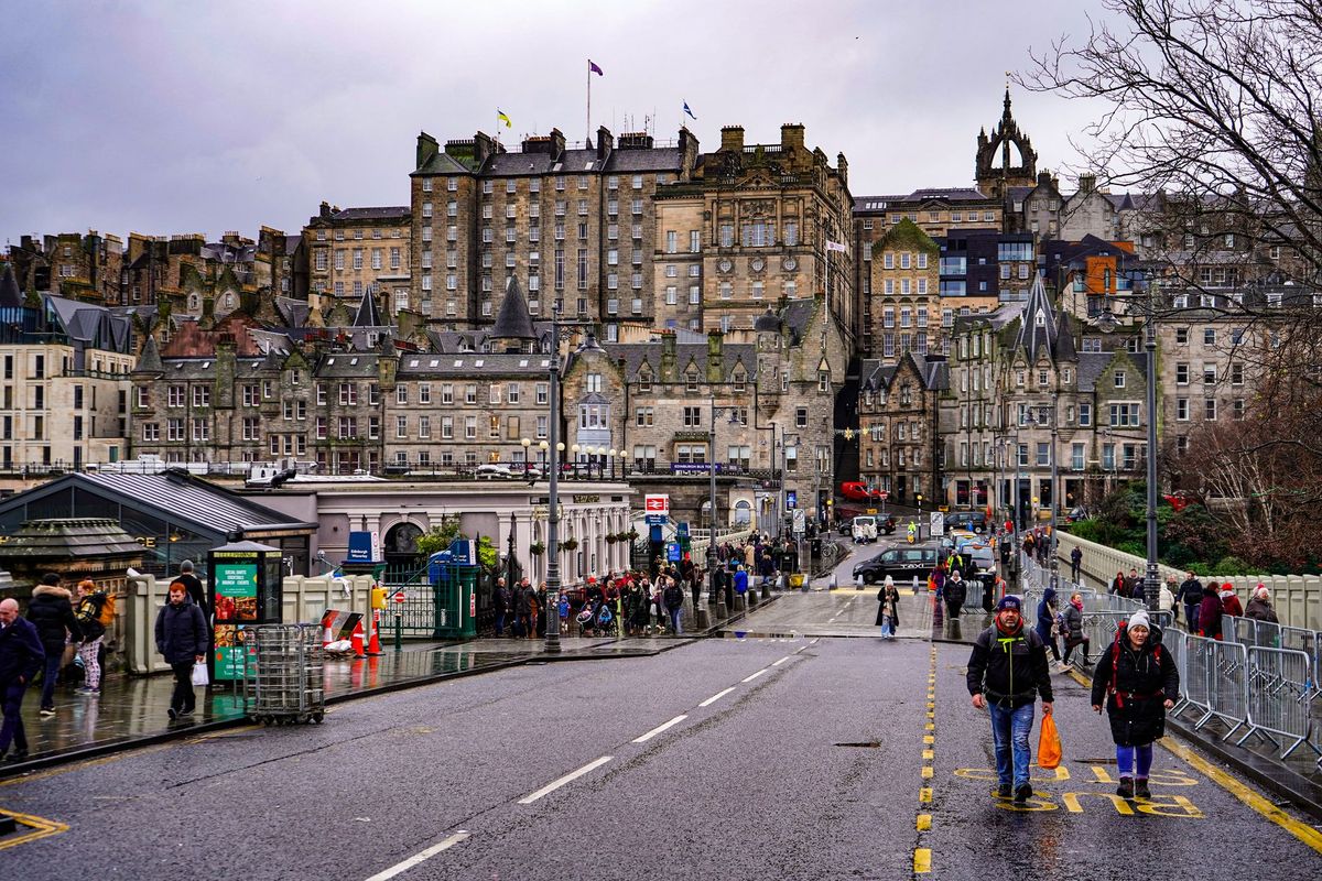 Pedestrians crossing the North Bridge in Edinburgh's Old Town on a grey, rainy day.