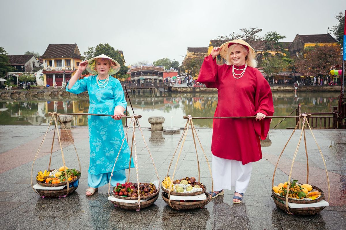 Tourists in ao dai carrying shoulder baskets by Hoi An's covered bridge